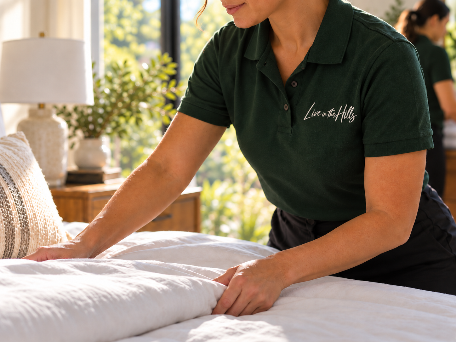Live in the Hills team member in an embroidered moss green uniform preparing fresh linens in a welcoming Los Angeles home